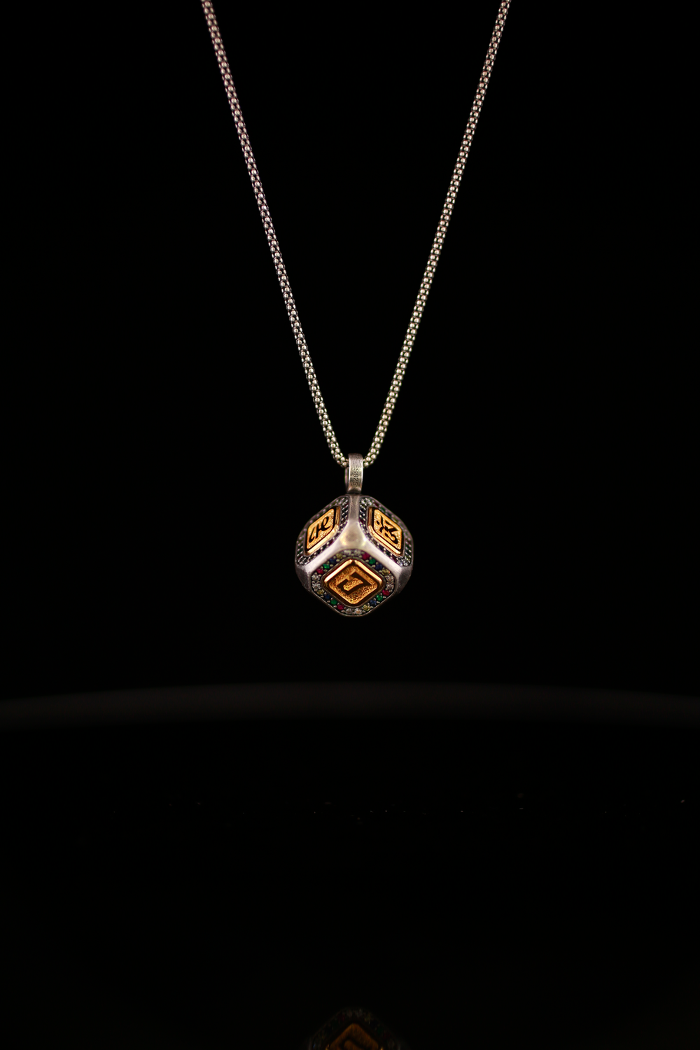 Six-Syllable Mantra Cube Pendant Necklace showing three gold tone inscribed panels on a dark cube against a black background