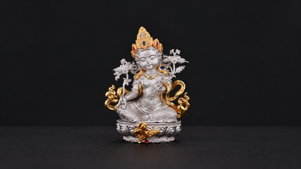 Silver-tone seated Green Tara figure with a gold-tone crown, shoulder flowers, lotus stems, curling ornaments, and pedestal fully visible against a dark background.