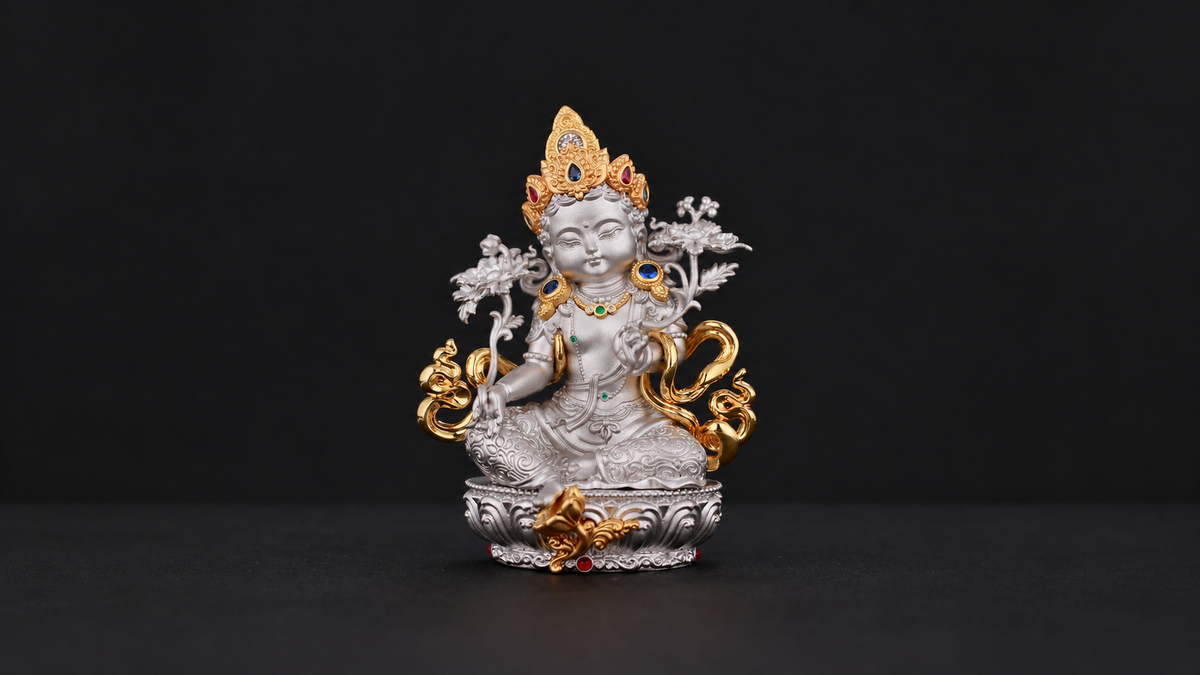 Silver-tone seated Green Tara figure with a gold-tone crown, shoulder flowers, lotus stems, curling ornaments, and pedestal fully visible against a dark background.