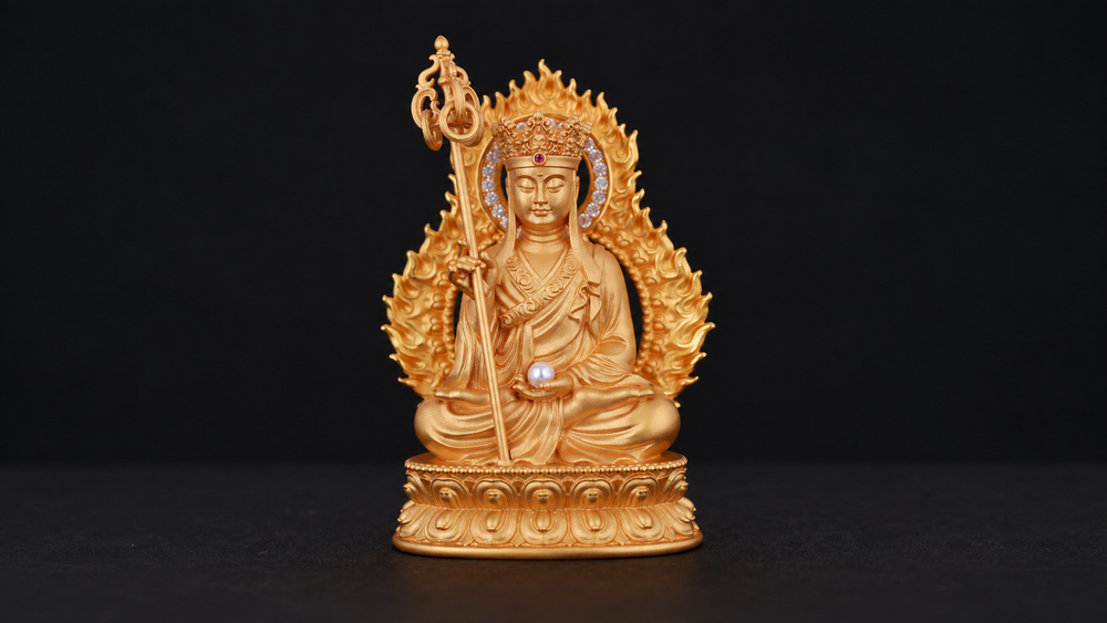 Gold-tone seated Ksitigarbha with a crown, ringed staff, pale orb, flame-shaped surround and double lotus pedestal, fully visible against black.