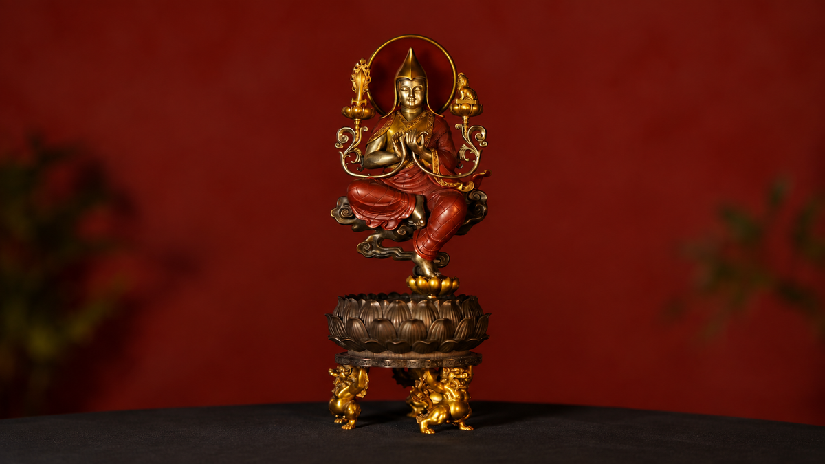 Tsongkhapa sculpture in red robes with a yellow hat, central teaching gesture, shoulder lotuses, and a layered lotus throne against a deep red background.