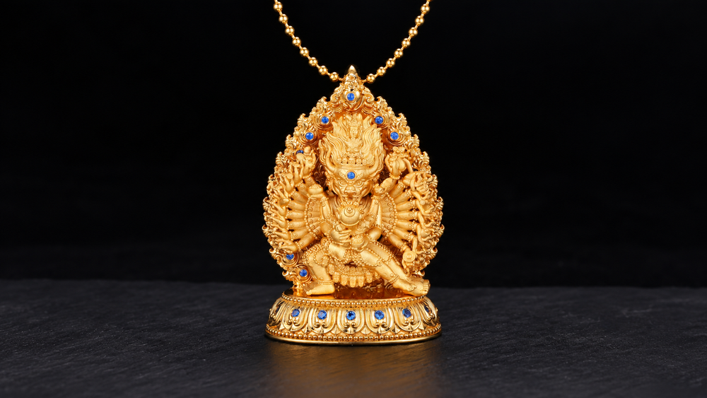 Gold-toned Daweide Yamantaka pendant with a horned face, radiating arms, blue accents and a lotus base, centered on dark stone.