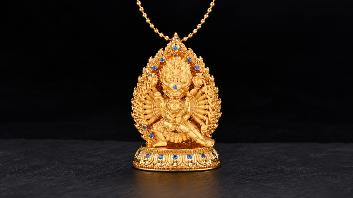 Gold-toned Daweide Yamantaka pendant with a horned face, radiating arms, blue accents and a lotus base, centered on dark stone.