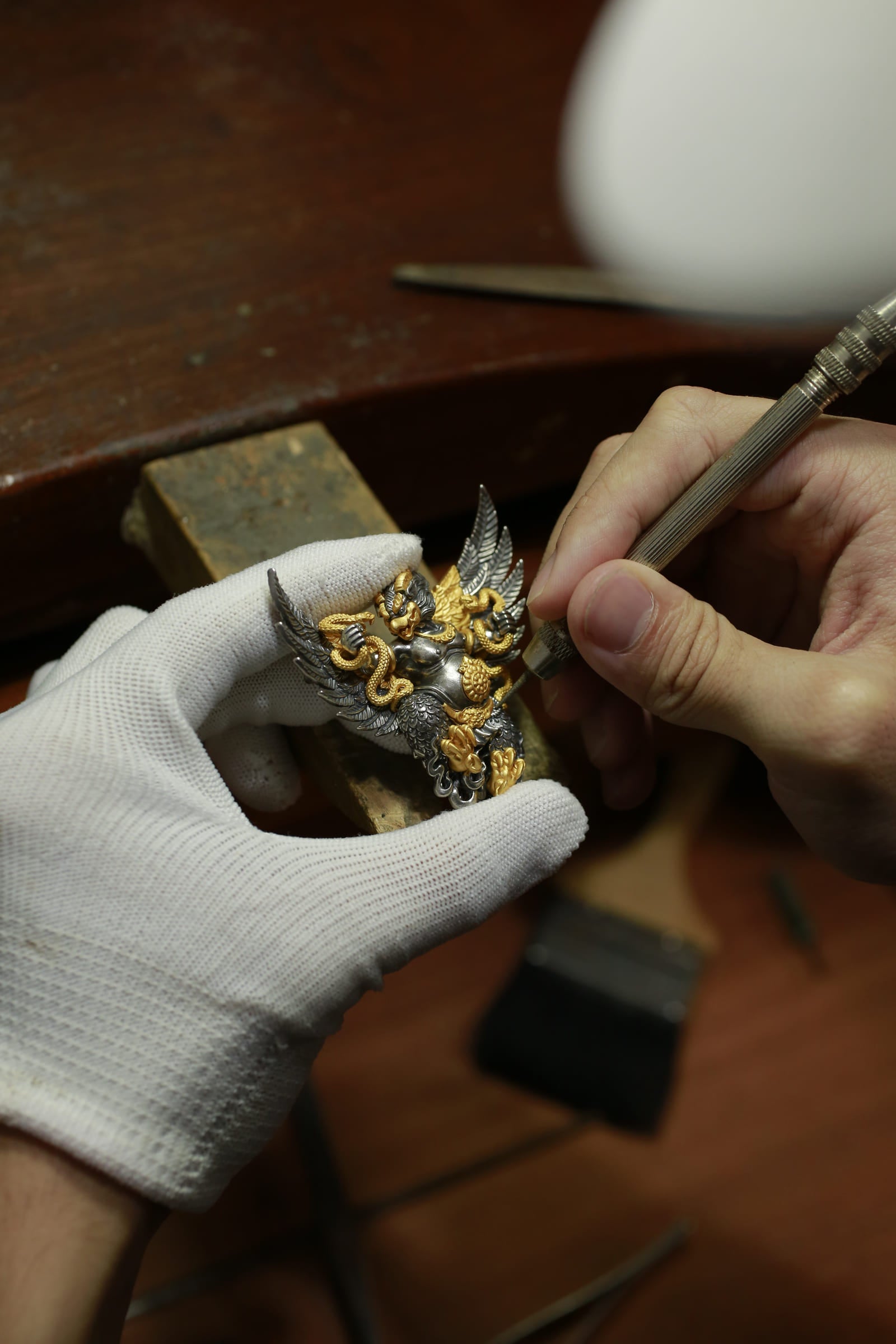 A Likreat artisan hand-carving a two-tone Garuda pendant